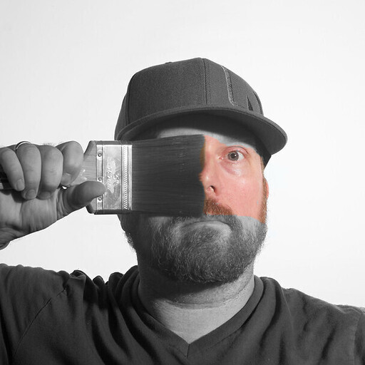 Man holding a paintbrush and swiping across face revealing color in an otherwise black and white photo.